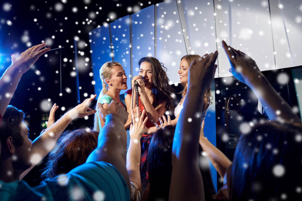 Happy young women singing karaoke on night club stage.