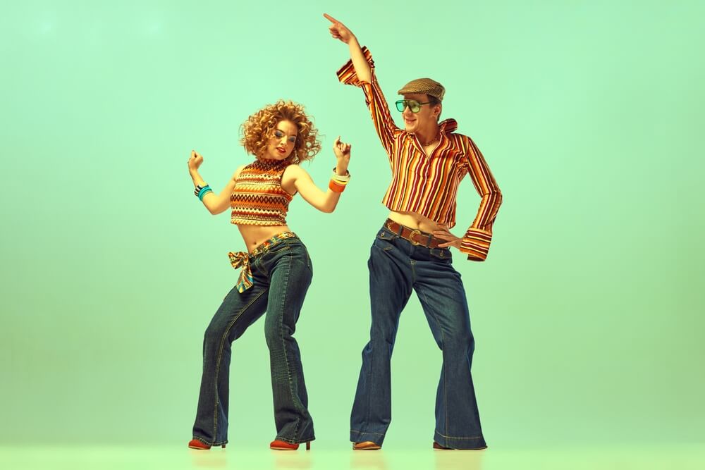 Two excited people, man and woman in retro style clothes dancing disco dance over green background.