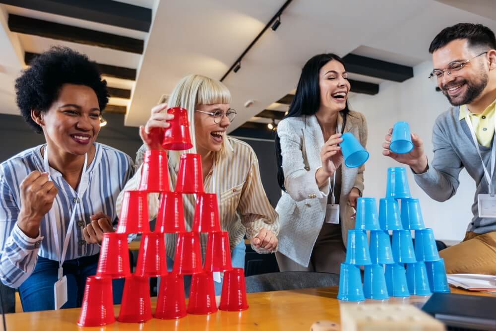 Group of young business people playing, building towers from plastic cups, two teams, blue and red.