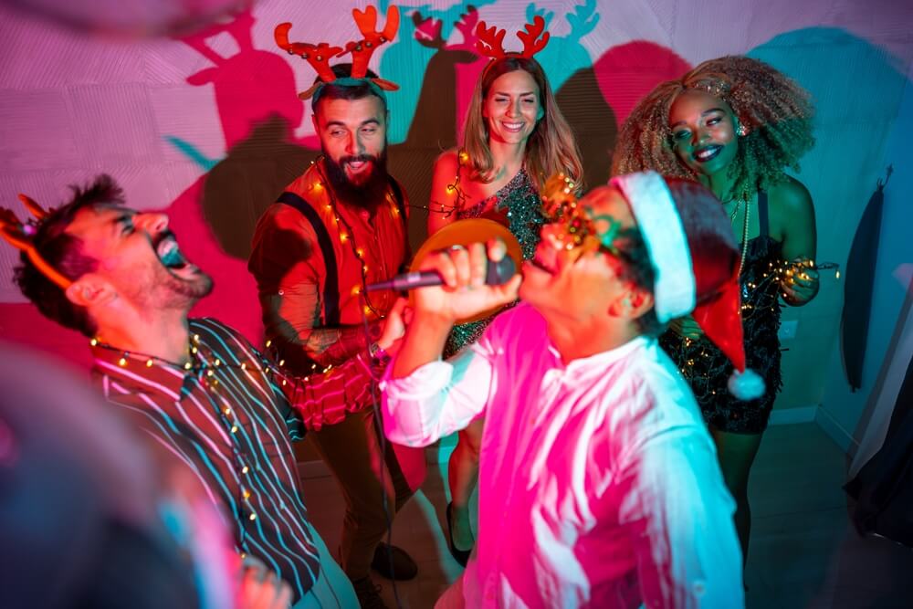 Group of cheerful young friends having fun singing karaoke and dancing at the Christmas party.