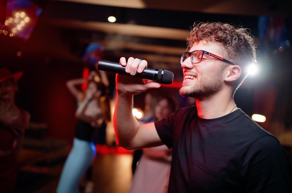 Happy young man singing at the karaoke party.