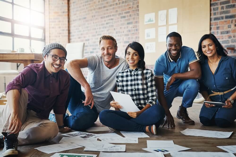 Group of people sitting on the floor in the office with paperwork or documents.