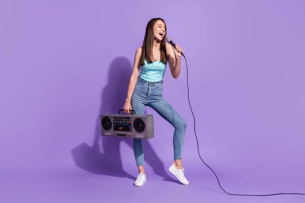 A young woman sing song microphone hold cassette player isolated on violet color background.