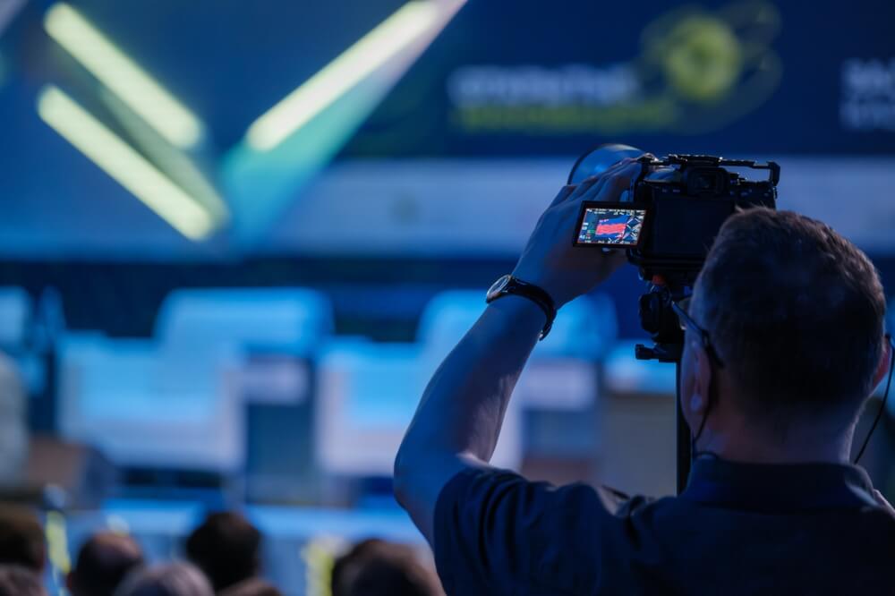 Professional videographer captures key moments at a corporate event, focusing his camera on a speaker amidst an attentive audience.